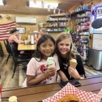Two girls smiling while holding ice cream cones inside the restaurant
