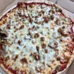 Cheese pizza with sausage and mushrooms in a takeout box