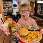 Boy excitedly holding trays of burgers, fries, and ice cream in restaurant
