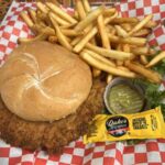 Fried chicken sandwich with fries and pickle on checkered paper