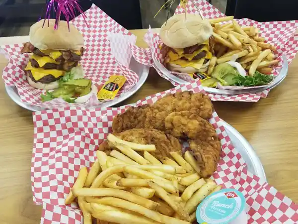 Fried chicken tenders with fries and cheeseburgers on checkered paper trays