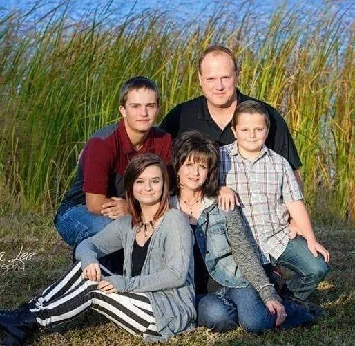 Family portrait of five people seated outdoors in tall grass