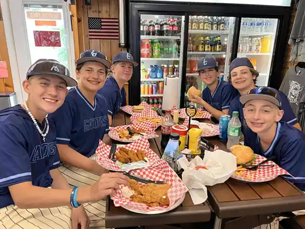 Group of boys in baseball uniforms eating lunch at a restaurant table
