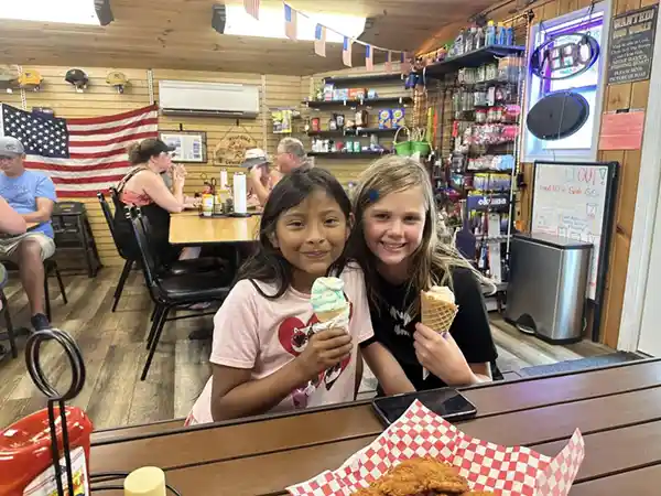 Two girls holding ice cream cones at a restaurant table