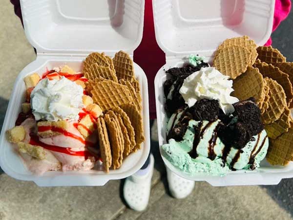 Two takeout ice cream sundaes topped with whipped cream and wafers